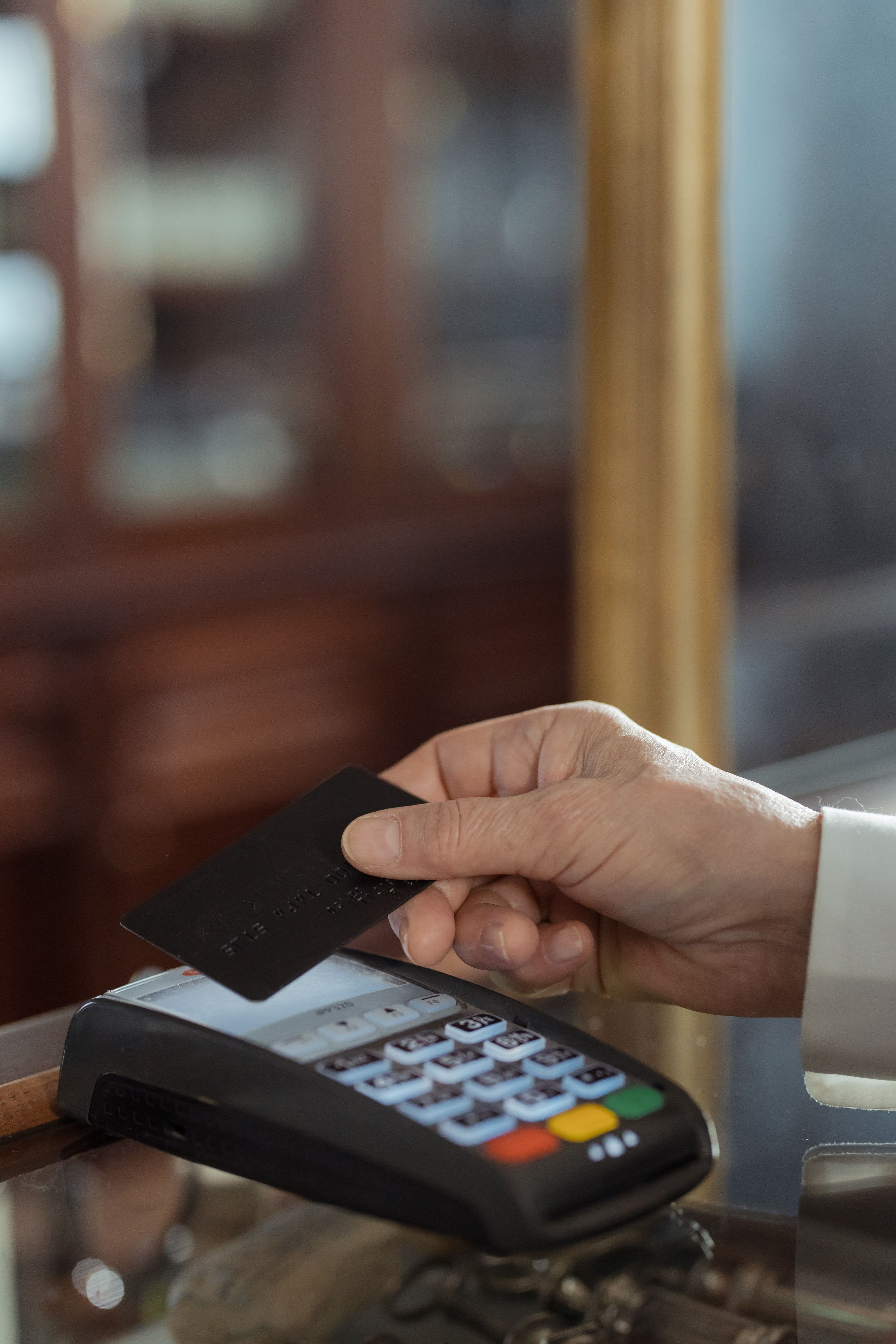 Hand holding a black credit card over a payment terminal for a contactless transaction.