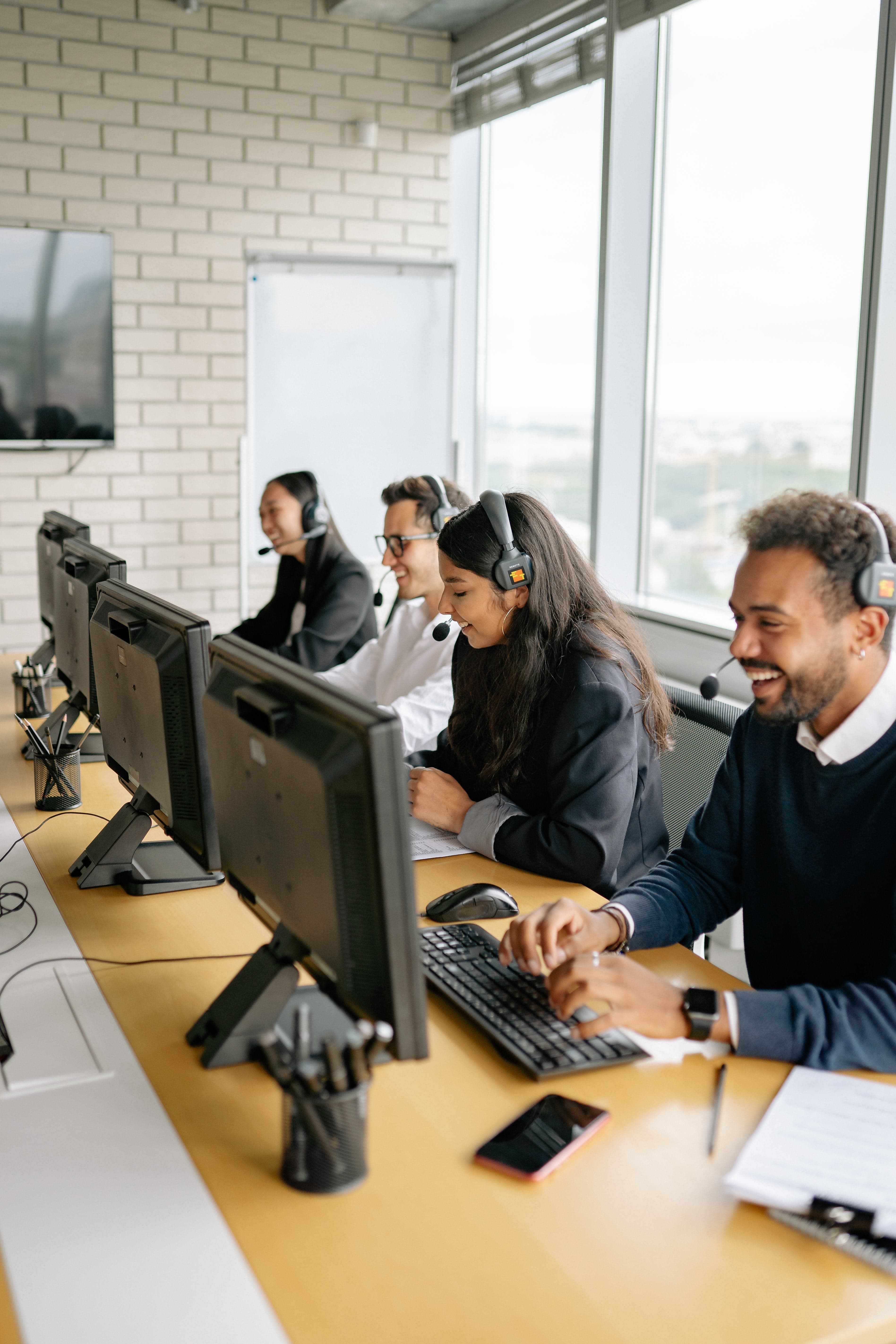 Diverse customer service team wearing headsets and smiling while working at computers in an office.