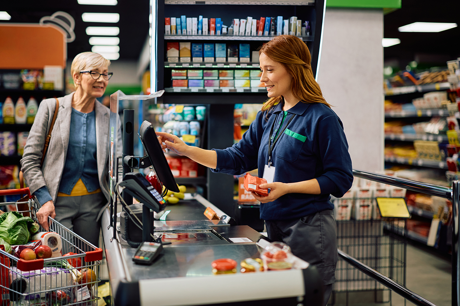Happy supermarket cashier scanning goods at store checkout.